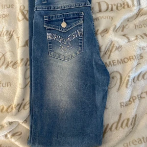 Blå bootcut jeans med broderade fickor - Snygga blå bootcut jeans med broderade detaljer på bakfickorna. Jeansen har en klassisk femficksdesign och en lätt tvättad look som ger en avslappnad stil. Säljer på grund av att dom inte kommer till användning. Jag är 160cm lång o dom passar mig. Fler frågor kontakta mig 🩷