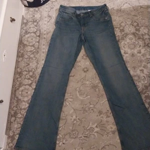 Blå bootcut jeans - Säljer ett par snygga blå bootcut jeans från &Denim. De har en låg midja och klassisk femficksdesign. Perfekta för en avslappnad stil.