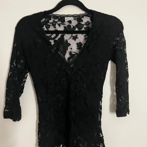 Svart spetsbody med trekvartsärm - Elegant svart spetsblus med v-ringning och trekvartsärmar. Vackra och feminina spetsdetaljer. 