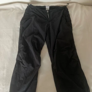 Svarta parachute pants  - Säljer ett par svarta byxor från Iets Frans i storlek S. Byxorna har en praktisk dragkedja framtill och är justerbar vid bensluten och midjan för en anpassad passform. De är använda men är fortfarande i bra skick. 