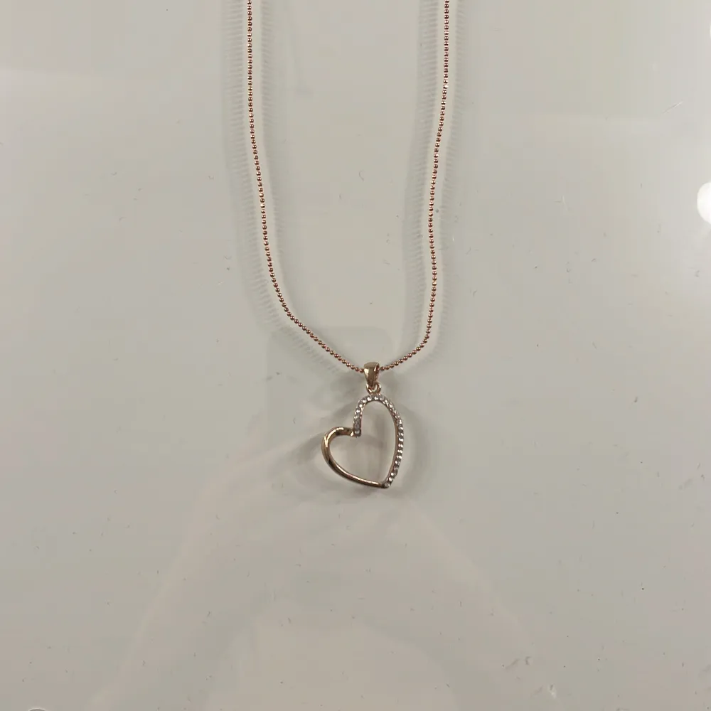 Ett guld halsband med en hjärtformad berlock. Som är ny och aldrig använd. Smycket kommer från Smycka.. Asusteet.