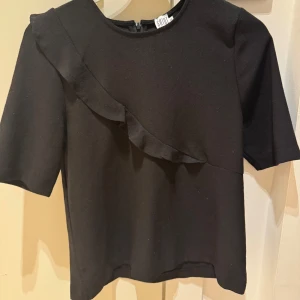Svart blus med volangdetalj - Fin topp med volang över bröstet, knappt använd❤️