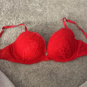 Röd spets-bh från Victoria's Secret - Säljer en röd push-up bh från Victoria's Secret med vacker spetsdetalj. Bh:n har justerbara axelband och ger ett lyxigt intryck. Perfekt för att känna sig extra fin.