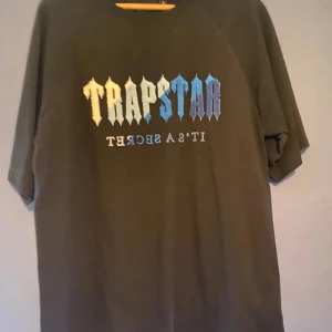 Svart t-shirt från Trapstar - Cool svart t-shirt från Trapstar med texten 'It's a Secret' i blå och vit gradient på framsidan. Perfekt för en avslappnad stil.