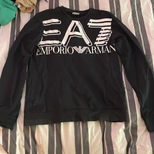 Svart tröja från Emporio Armani - Snygg svart tröja från Emporio Armani med stort EA7-tryck på framsidan. Herr modell storlek S. Väldigt bra skick använd fåtal ggr. Skriv vid intresse eller mer info. Köparen betalar frakt. 