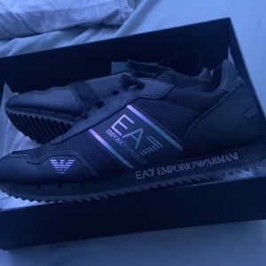 Svarta sneakers från Emporio Armani - Snygga svarta sneakers i storlek 40 från Emporio Armani med EA7-logga på sidan. Dom är i mycket bra skick och har haft användning 2-3 gånger, de är nästan oanvända . Hör av dig om du är intresserad! Lådan följer med!