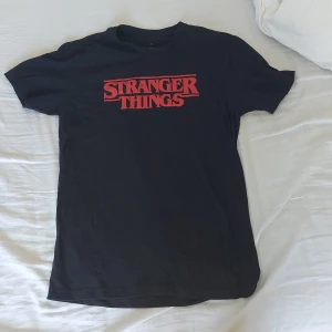 Svart Stranger Things t-shirt från Netflix - Säljer en svart Stranger Things t-shirt från Netflix i storlek M. Den är gjord av 100% bomull och är superbekväm. Perfekt för alla Stranger Things-fans! T-shirten har korta ärmar och en normal passform. Den är i nyskick och har bara använts ett par gånger. Köp den nu och visa din kärlek för serien! ❤️🖤
