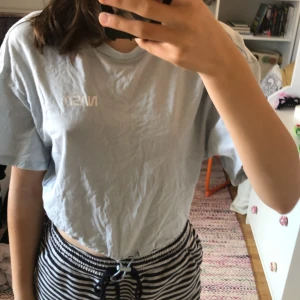 Ljusblå t-shirt med tryck från Pull&Bear - Säljer en superfin ljusblå t-shirt/magtröja från Pull&Bear. Den har ett coolt tryck på framsidan med texten 'NASA' och på baksidan står det 'WITH LOVE FROM PLANET EARTH' tillsammans med några fredssymboler och en astronaut. T-shirten är i storlek XS och är i bra skick. Perfekt för träning med bekväm stil!