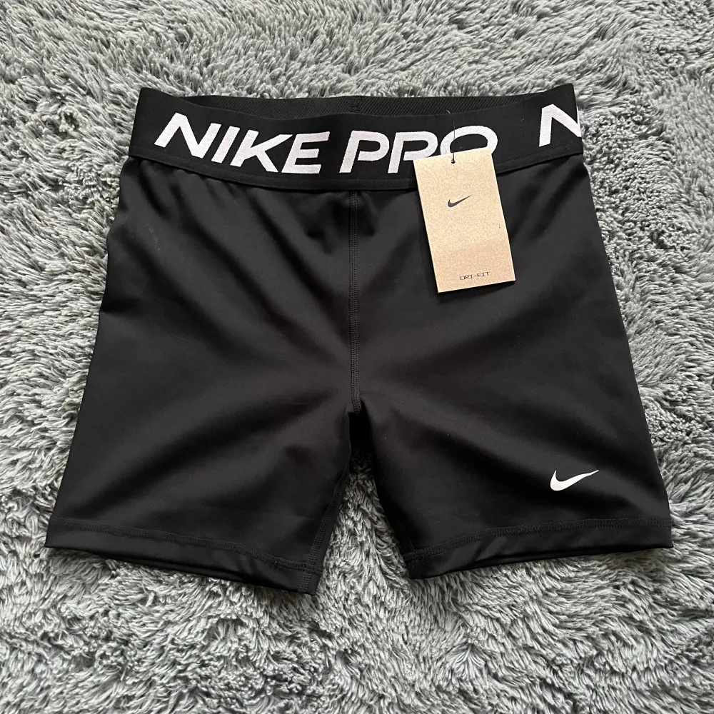 Säljer ett par svarta träningsshorts från Nike Pro. De är i nyskick, aldrig användna med lappen på och har en tight passform. Shortsen är gjorda av polyester och har en bred resår i midjan med Nike Pro-loggan. köpt för 300kr. skriv för fler bilder eller frågor!. Shorts.