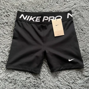 Svarta träningsshorts från Nike Pro - Säljer ett par svarta träningsshorts från Nike Pro. De är i nyskick, aldrig användna med lappen på och har en tight passform. Shortsen är gjorda av polyester och har en bred resår i midjan med Nike Pro-loggan. köpt för 300kr. skriv för fler bilder eller frågor!