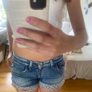 Blå jeansshorts från Wendy Brand - Säljer ett par snygga blå jeansshorts från Replay. De är lågmidjade och har en hyfsat tight passform. Shortsen har en söt blommig kant längst ner som ger dem en unik touch, men den går även att vika in (bild2). 🌸