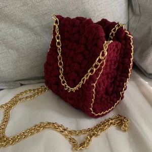 Vinröd stickad handväska med guldkedja - Säljer en superfin Petite vinröd stickad handväska med en snygg guldkedja som axelrem. Väskan är perfekt för både vardag och fest och ger en mysig men ändå elegant look. Den är i nyskick och redo att användas direkt. Passa på att köpa denna unika väska! 💖