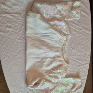 Vit tröja med paljetter från H&M - Säljer en superfin vit tröja från H&M med glittriga paljetter på ärmarna. Tröjan är perfekt för festliga tillfällen och har en normal passform. Den är i bra skick och redo för en ny ägare. Passar perfekt till både jeans och kjol!