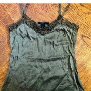 Grön linne topp från H&M - Säljer en snygg grön linne topp från H&M. Toppen har tunna axelband och vacker spetsdetalj runt halsringningen. Perfekt för sommaren eller en festkväll. 