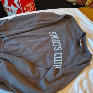 Grå sweatshirt med texten 'SPORTS CLUB' - Säljer en grå sweatshirt med texten 'SPORTS CLUB' tryckt på framsidan. Tröjan är i storlek M och har långa ärmar. Perfekt för en avslappnad stil eller för att bära till träningen. Den är i bra skick och väldigt bekväm. Passar både höst och vinter.