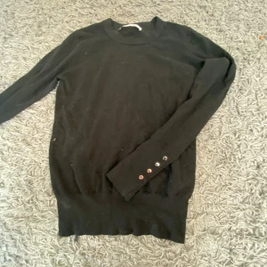 Svart långärmad tröja med knappar - Säljer en svart långärmad tröja med knappar på ärmsluten. Tröjan är enkel och stilren, perfekt för höst och vinter. Den är i bra skick och passar till både vardag och fest. Materialet känns mjukt och bekvämt. made in chinesw