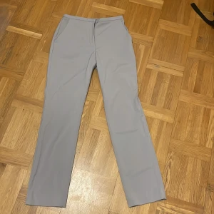 Grå kostymbyxor från H&M - Säljer ett par stilrena grå kostymbyxor från H&M i storlek 36. Byxorna har en hög midja och raka ben, vilket ger en klassisk och elegant look. Perfekta för både kontoret och mer formella tillfällen. De är i mycket bra skick och har praktiska fickor fram. Köparen står för frakten!