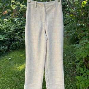 NA-KD byxor tall - Ett par beige högmidjade byxor från NA-KD med linnestruktur (50% bomull och 50% polyester). Använda några gånger därav lite noppigt runt fickorna. Långa i modellen. 