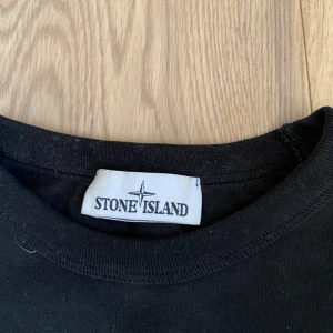 Svart tröja från Stone Island - Säljer en svart tröja från Stone Island. Tröjan är i bra skick och har en klassisk design med Stone Island-loggan på vänster ärm. Den är långärmad och gjord av bomull, vilket gör den både bekväm och stilren. Perfekt för höst och vinter!
