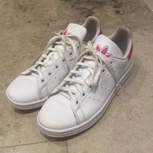 Vita Adidas Stan Smith sneakers med rosa detaljer - Säljer ett par vita Adidas Stan Smith sneakers i storlek 37 1/3. Skorna är köpta i början av sommaren så därför i bra skick med några mindre tecken på användning💕(säljer på fler ställen, kontakta mig) 