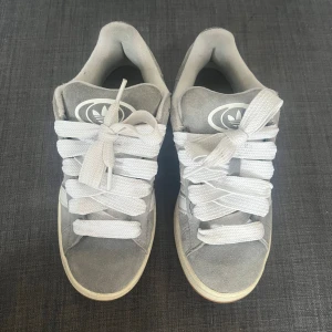 Gråa Adidas Campus sneakers - Säljer ett par gråa Adidas Campus 00s sneakers. De är i bra skick och det medföljer även extra skosnören😊
