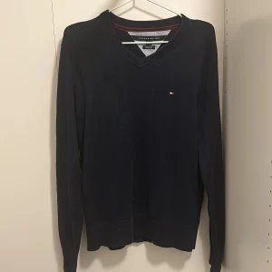 Mörkblå tröja från Tommy Hilfiger - Säljer en snygg mörkblå tröja från Tommy Hilfiger i storlek S. Tröjan är gjord av mjuk Pima bomull och har en v-ringad hals. Perfekt för både vardag och fest. Den är i bra skick och har långa ärmar. Passar perfekt till höst och vinter! Dm för fler funderingar.