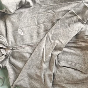 Grå hoodie från Nike - Säljer en grå hoodie från Nike i storlek S. Den har en dragkedja framtill och är tillverkad i bomull. Perfekt för vardagsbruk eller träning. Hoodien är i välanvänt skick med lite slitage vid ärmsluten.