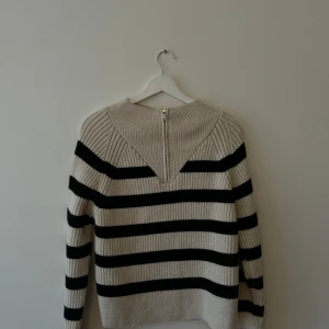 Randig stickad tröja från Zara - Säljer en superfin randig tröja från Zara i storlek M. Den är stickad och har en snygg kombination av beige och svart ränder. Tröjan har långa ärmar och en dragkedja i nacken för en cool detalj. Perfekt för höst och vinter!