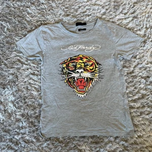 Grå t-shirt med tigertryck från Ed Hardy - Säljer en grå t-shirt från Ed Hardy med ett coolt tigertryck på framsidan. T-shirten är kortärmad och i bomull, perfekt för en avslappnad stil. Passar bra till både jeans och shorts! 