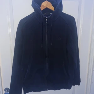 Hugo Boss Zip Hoodie - Svart hugo boss hoodie i storlek L men sitter mer som M, köpt här på plick så har inte kvitto. Har ett litet hål i en innerficka men jag kan laga hålet vid behov. Jag är 192 75kg och den var lite kort i armarna