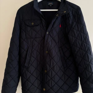 Mörkblå Ralph Lauren quiltad jacka - Skit snygg jacka från Ralph Lauren! Säljs för att jag inte använder den, har använts kanske 5-10 gånger. Perfekt skick. Nypris cirka 3500kr men säljer för 999kr. Perfekt till hösten. Hör gärna av dig vid pris förslag eller annat!