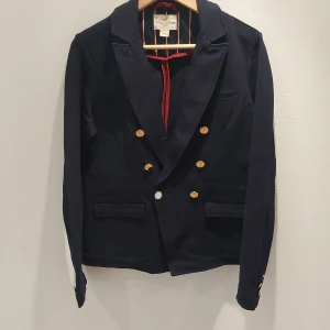 Svart kavaj från Holly & Whyte - Säljer en stilren marinblå kavaj från Holly & Whyte by Lindex. Kavajen har en klassisk design med dubbla knapprader i guld och en snygg krage. Perfekt för både vardag och fest! 🖤