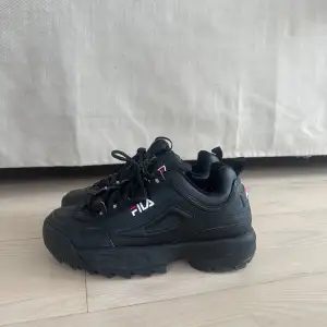 Säljer ett par svarta Fila Disruptor sneakers. Använd fåtal gånger men har fått skav på sidan. De har en chunky sula. Skorna har snörning framtill och Fila-loggan syns både på sidan och baksidan. Perfekta för en casual look! 