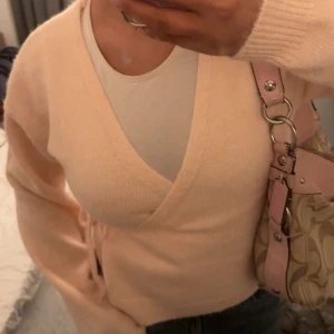 Persikofärgad omlottkofta - Säljer en mysig beige omlottkofta med knytband i midjan. Koftan har långa ärmar och en v-ringad design, perfekt för lager-på-lager outfits✨så fin nu till hösten och suuuperskön💕💕