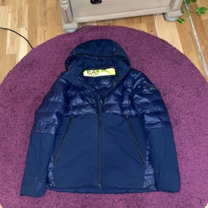 Mörkblå jacka från Emporio Armani - Snygg mörkblå jacka från Emporio Armani med huva och dragkedja. Perfekt för kyligare dagar med sin stilrena design.
