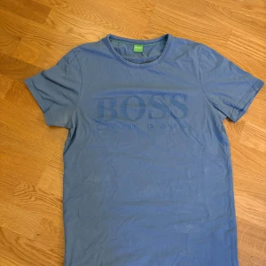 Hugo Boss T-shirt - Snygg blå t-shirt från Hugo Boss med subtilt broderad logga på bröstet. Perfekt för en avslappnad stil. Kortärmad och tillverkad i mjukt material för extra komfort.