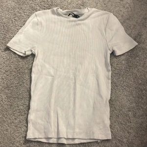 Vit ribbad t-shirt från BIK BOK - Säljer en stilren vit ribbad t-shirt från BIK BOK i storlek XS. Perfekt basplagg med korta ärmar och en bekväm passform. Passar till alla tillfällen!