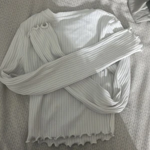 Vit ribbad tröja från FB Sister - Säljer en vit ribbad tröja från FB Sister i storlek XXS. Tröjan har långa ärmar och en vågig kant vid nederdelen som ger en fin detalj. Perfekt för en stilren look.