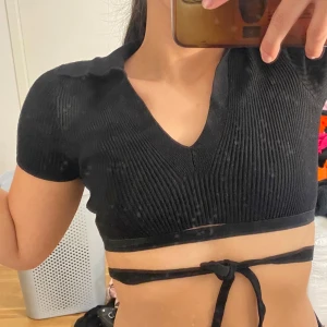 Svart ribbad croppad topp från Sister Knitwear - Snygg svart ribbad topp från Sister Knitwear i storlek XS. Den är croppad med en v-ringad design och har korta ärmar. 