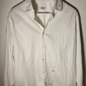 Vit skjorta från Moschino - Klassisk vit skjorta från Moschino med knappar framtill. Perfekt för en stilren look. Skjortan har långa ärmar och en krage som ger en elegant touch.