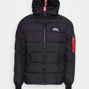 Alpha Industries Jacka - Snygg svart pufferjacka från Alpha Industries med huva och dragkedja. Jackan har en broderad logga på bröstet och en röd detalj på ärmen. Perfekt för kyliga dagar. Skriv för mer bilder, och skick osv 😁