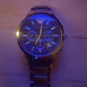 Emporio Armani herrklocka - Snygg herrklocka från Emporio Armani med blå urtavla och silverfärgad metallarmband. Klockan har tre små urtavlor och datumvisning. Perfekt för den stilmedvetne, och för den som helt enkelt älskar att bara snygg