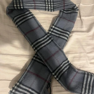 burberry halsduk  - Snygg grå halsduk med klassiskt rutigt mönster i svart och vitt. Perfekt för att hålla sig varm under kyliga dagar. Den har en stilren design som passar till många olika outfits. Hör av er vid intresse😄