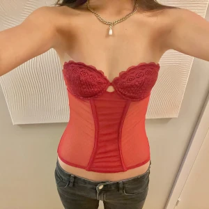 Korsett topp - Snygg röd axelbandslös korsett med spetsdetaljer och transparenta partier. Perfekt för en kväll ute eller en speciell tillställning. 
