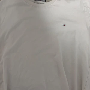 Vit t-shirt från Tommy Hilfiger - Säljer en klassisk vit t-shirt från Tommy Hilfiger med en liten logotyp på bröstet. T-shirten är kortärmad och tillverkad i bomull, perfekt för en stilren look.