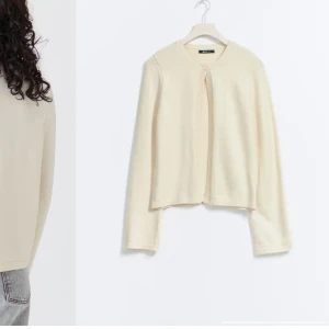 Beige kofta från gina - Säljer en stilren beige kofta från gina. Koftan har en enkel design med rund hals och långa ärmar. Perfekt för lager-på-lager under kyligare dagar.