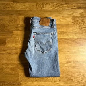 Blå jeans från Levi's - Säljer ett par klassiska blå jeans från Levi's med slitna detaljer på framsidan. De har en rak passform och är tillverkade i denim. De är sydda 1 gång vid inner lårbenet men syns knappast. Storleken W28 L30 och Lot 512, skriv vid frågor eller funderingar mvh.