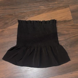 Svart tube top med volang - Trendig svart tubetop med volangdetalj i nederkant. Enkel och använt ett fåtal gånger så den är i bra skick.