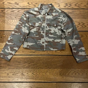 Camouflage jacka med dragkedja - Säljer en tunn fin jacka från Lindex med dragkedja och två bröstfickor. Perfekt nu inför kommande vår. Jackan är croppad och har en klassisk krage. Perfekt för en cool och avslappnad stil. Från rök/djurfritt hem. Stlk: S