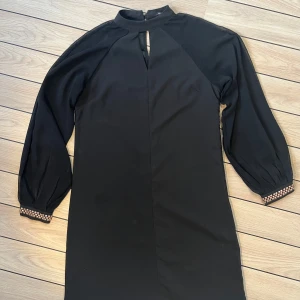 Svart kort klänning  - Genomskinliga ärmar med metalldetaljer. 